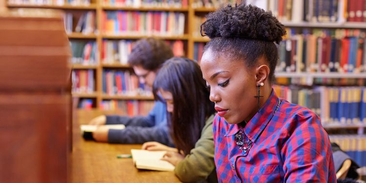 Student at a desk surrounded by shelves of books.