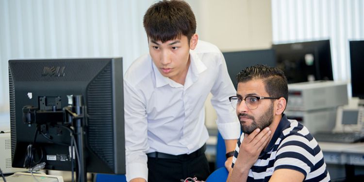 Someone at a desktop with another person reviewing their screen while standing next to them.