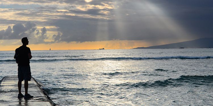 A silhouette of someone stood facing the sea.
