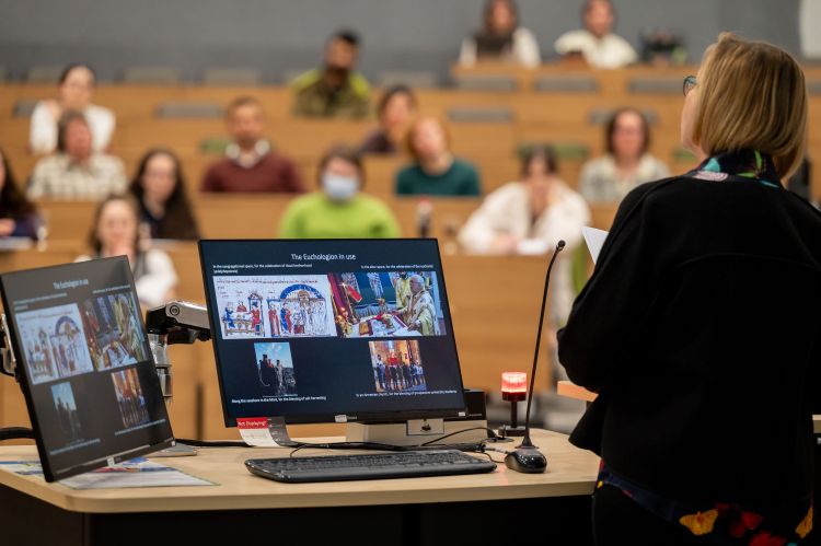 Claudia Rapp standing at a lectern in front of the lecture audience