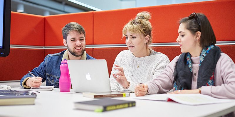 Three students in a library booth discussing works,