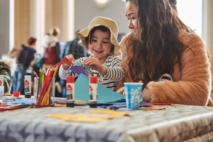 Parent and child making paper crafts with glue, crayons and coloured paper.