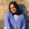 MA FAHACS student Rachel Noronha headshot image. Rachel stands in front of a brick wall and is smiling. She wears a purple cardigan and white t shirt.