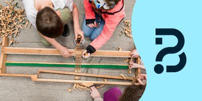 From above, four children putting the pieces of the inside of a piano together. On the right is the Be Curious logo.