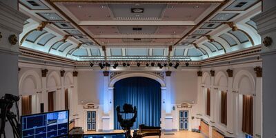 Technology desk in the Clothworkers Centenary Concert Hall based on the balcony, looking down at the stage area where a piano is placed.
