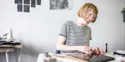 Artist Lucy Crouch in the studio. Lucy is drawing at a desk and there are drawings attached to the back wall.