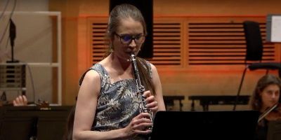 Heather Roche performing in an ensemble at a festival. The image captures her playing her instrument with other musicians to the left and right.