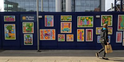 Person walking in front of a building site hoarding which is covered in colourful artwork.
