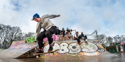 Skateboard doing skateboard tricks in the a skatepark with fellow skateboarders watching in the background.