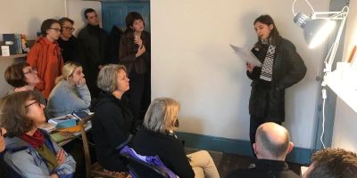 A person standing is giving a spoken word reading to a seated audience