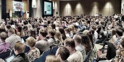A conference hall with lots of people facing the stage