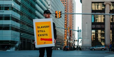 A person standing on the pavement in front of high rise building, with a sign that says 