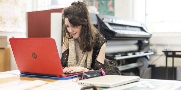 Student on laptop in front of large printer in a studio