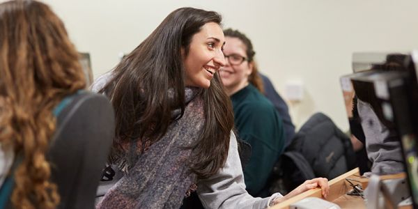 Students leaning over rows of computers to have a discussion.