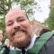 Harry smiling wearing a graduation gown and standing outside the Great Hall on campus.