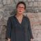 Profile image of Layla Khoo (a woman with short dark hair and red glasses) standing against a brick wall
