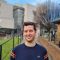 A picture of Shmuel wearing a blue jumper and standing outside Roger Stevens building