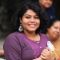 School of Fine Art, History of Art and Cultural Studies alumnus, Shreeja Mandal. Shreeja is looking to the left of the frame and is smiling. In the background two people are situated in the right of the frame and are out of focus.