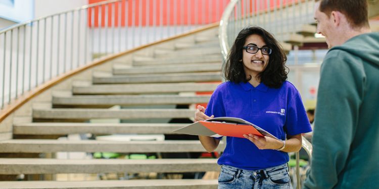 Student with a clipboard working for the university in branded tshirt helping another student.