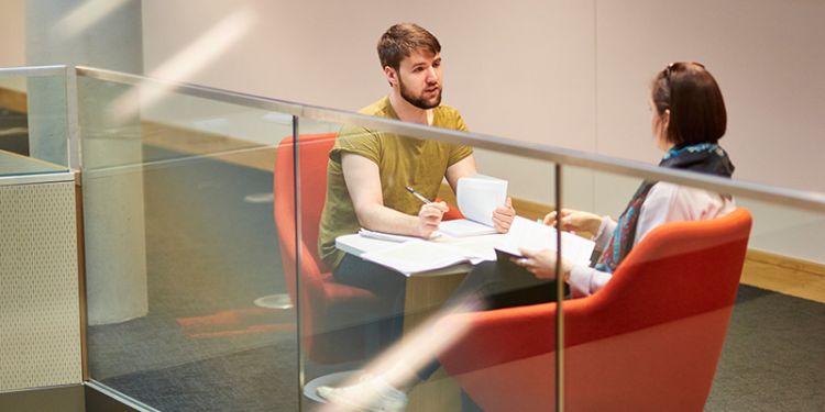 Two students sat on armchairs chatting