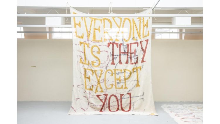 George's artwork at the MA show in 2024: a large painted wall hanging reads 'Everyone is they except you'