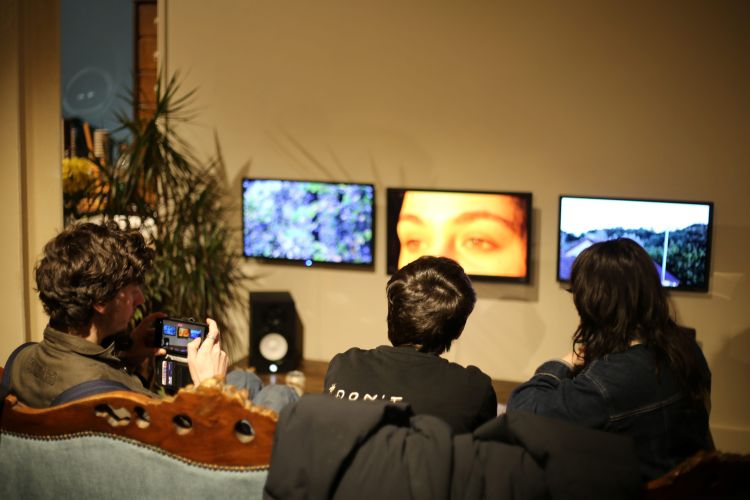 Three people seated watch a three screen audio visual installation