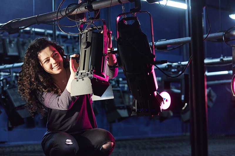 student on a lighting rig with a smiling face